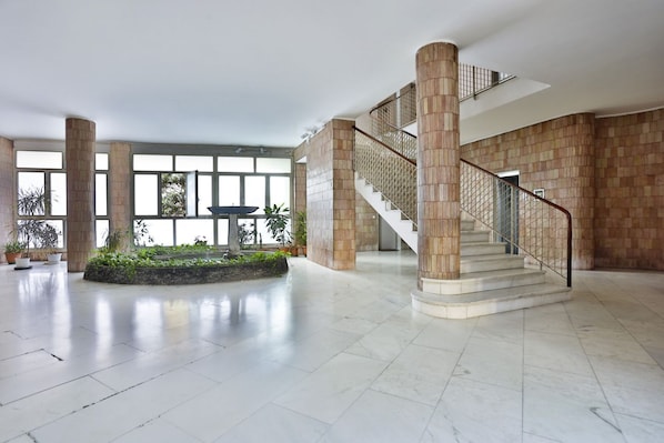 A spacious lobby with a central staircase, large windows, and potted plants.