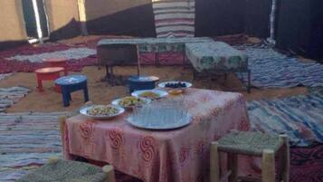 An outdoor dining area with a table set for a meal, surrounded by low stools and covered with a patterned tablecloth.