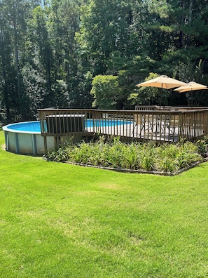 A backyard with a swimming pool, wooden deck, and outdoor seating area.