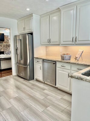 A kitchen with white cabinets, stainless steel appliances, and a herringbone-patterned floor.