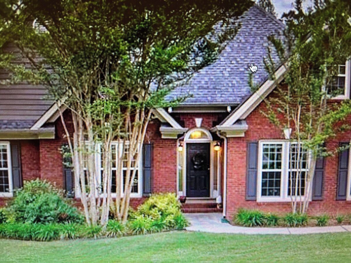 A brick house with a dark front door, white window shutters, and a small porch.