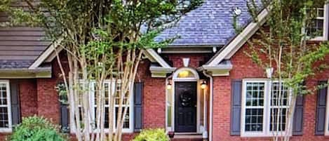 A brick house with a dark front door, white window shutters, and a small porch.