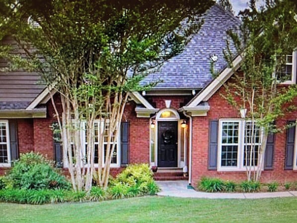 A brick house with a dark front door, white window shutters, and a small porch.