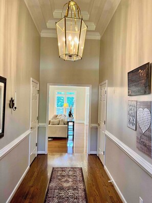 A hallway with a chandelier, a rug, and a bed in the background.