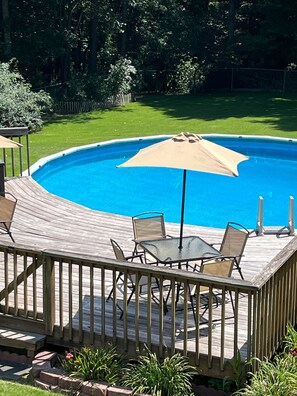 Una piscina con bordo in legno, circondata da un prato e una recinzione in legno.