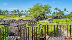 A tropical landscape with a metal gate, lush greenery, and a clear blue sky. - Kolea Villas 15M, Luxury, Direct Beach Access (Waikoloa)