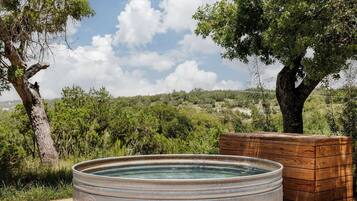 Relax in a hot tub on a wooden deck surrounded by trees and shrubs.