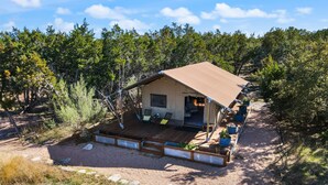 A cabin with a covered deck, surrounded by trees and a gravel path.