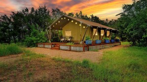 A tented accommodation with a covered deck, surrounded by greenery.