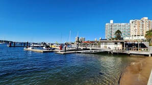 A waterfront marina with boats docked, a pedestrian bridge, and high-rise buildings in the background.