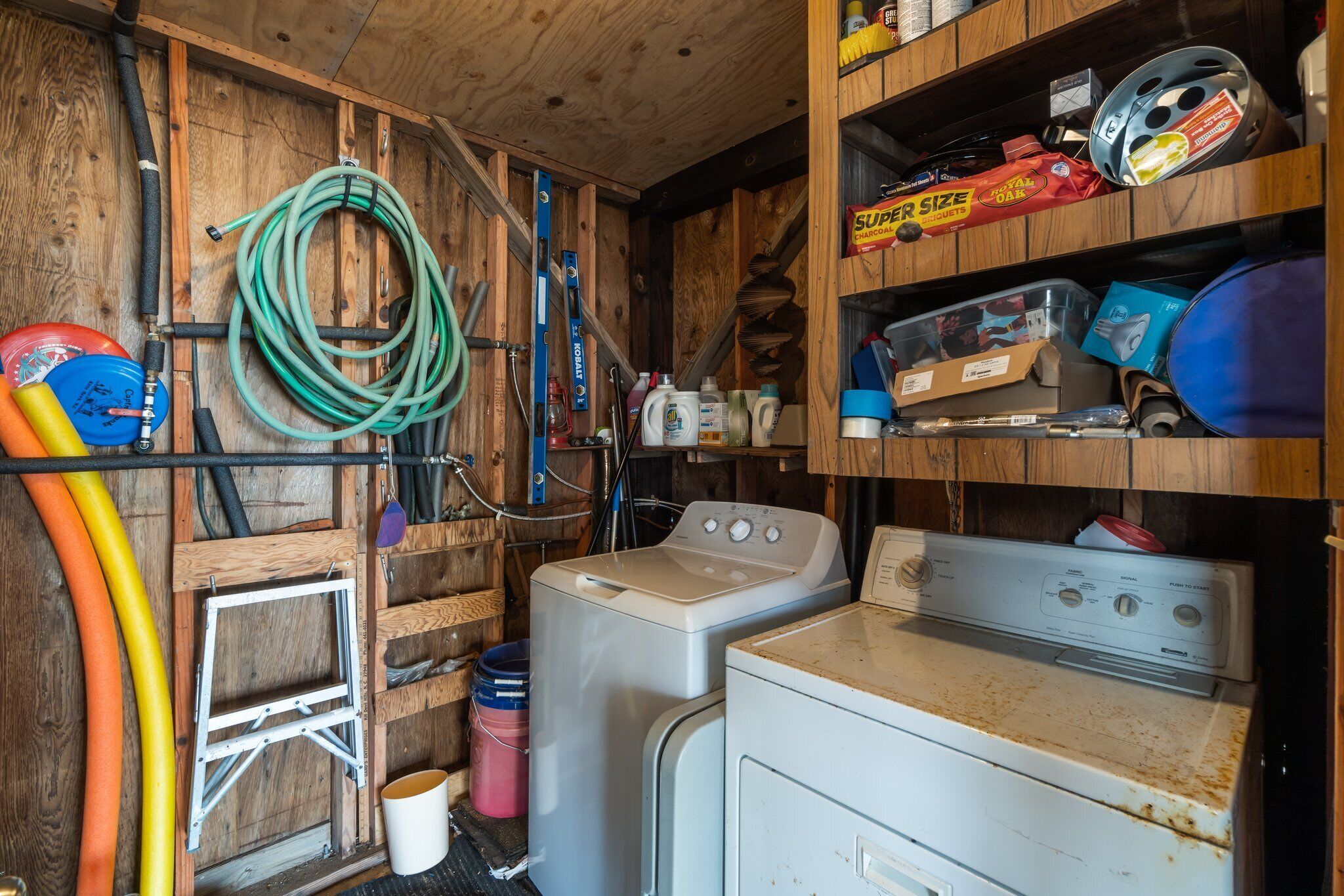 A laundry room with wooden walls, a washing machine, a dryer, and various cleaning supplies.