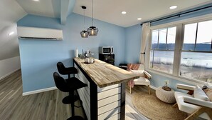 Cocina moderna con barra de madera, taburetes negros y un amplio ventanal con vista a un estacionamiento.