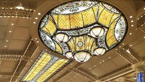 Interior de un casino con máquinas tragamonedas, una gran lámpara de candelabro y un techo alto con detalles ornamentales.