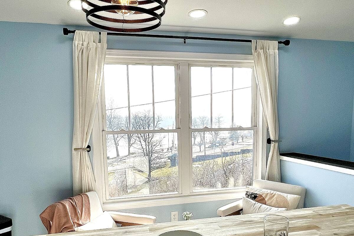 A modern kitchen with a wooden countertop, a hanging light fixture, and a window with curtains.