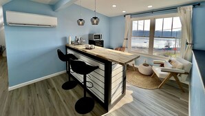 Cocina moderna con encimera de madera, taburetes negros, microondas y ventana con vista a un cuerpo de agua.