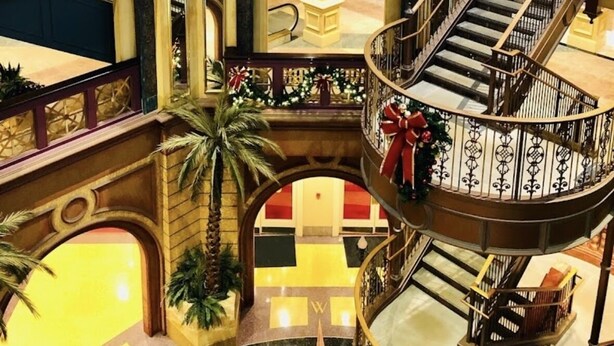 Un atrio de varios niveles con una escalera central, barandillas decorativas y vistas al área de la recepción.