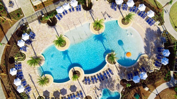 Luchtbeeld van een resort met een centraal zwembad, omringd door loungegedeeltes met parasols en ligbedden.