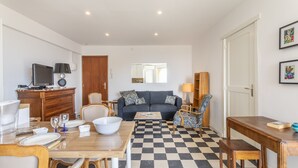 Un salon avec un sol à carreaux, un canapé, une table à manger avec des chaises, un téléviseur et un meuble en bois.