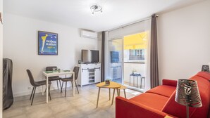 A modern apartment with a dining area, a kitchen, a living room with a red sofa, and a balcony with a yellow awning. - Studio Baldosa - Welkeys (Bandol)