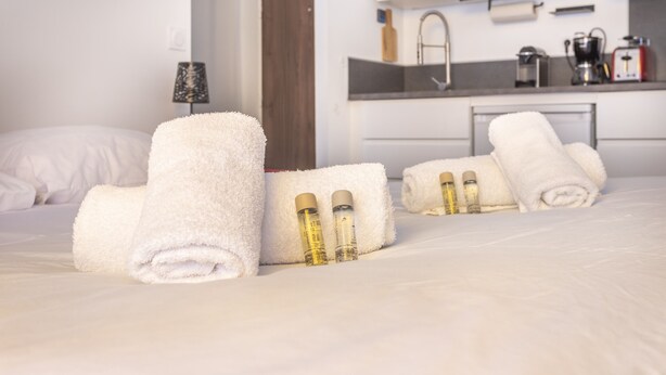 A neatly made bed with rolled white towels and two bottles of lotion. - Studio Baldosa - Welkeys (Bandol)