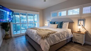Un dormitorio con una cama grande, una mesita de noche con lámpara y un televisor montado en la pared.