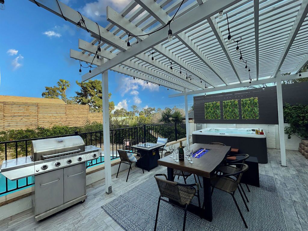 Een terras buiten met een barbecue, eettafel, stoelen en een hottub.