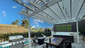 Un patio al aire libre con una parrilla, mesa de comedor, sillas y un jacuzzi.
