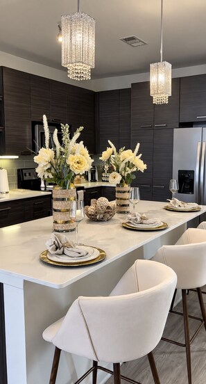 A modern kitchen with dark cabinetry, a marble countertop, and a central island with a dining setup.