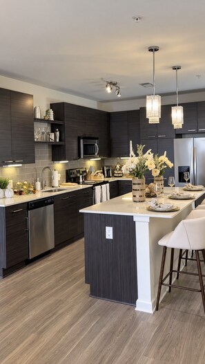 A modern kitchen with dark cabinetry, stainless steel appliances, and a central island with seating.