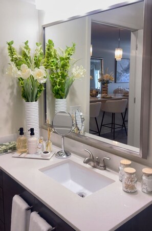 A bathroom with a large mirror, a sink, and two vases with flowers. - Atlanta Beltline Luxury Suite (Atlanta)