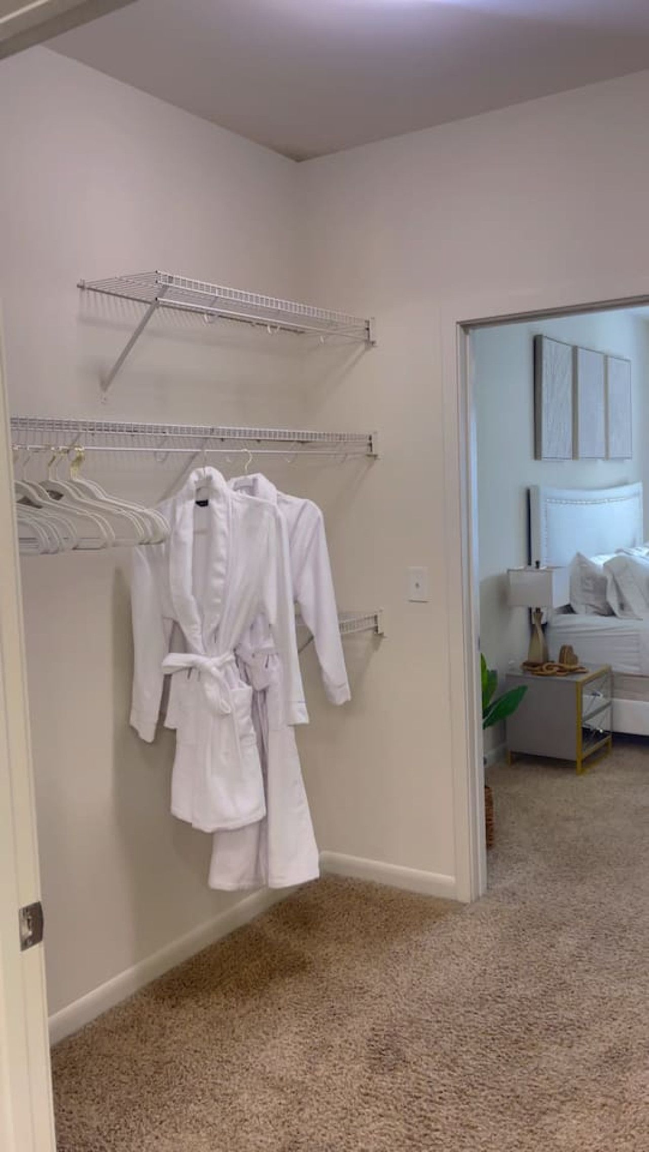 A room with a white robe hanging on a rack, a bed with white bedding, and a small bedside table with a lamp.