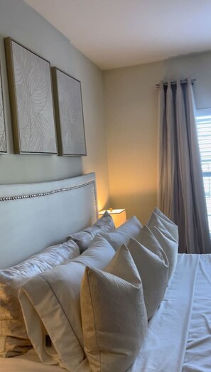 A bedroom with a bed, pillows, a headboard, a nightstand, a lamp, and a window with curtains. - Atlanta Beltline Luxury Suite (Atlanta)