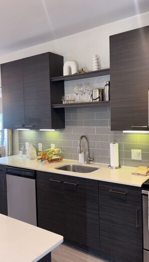 A modern kitchen with dark cabinetry, a stainless steel sink, and a countertop with various items. - Atlanta Beltline Luxury Suite (Atlanta)