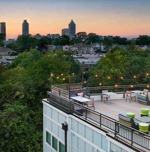 Eine Dachterrasse mit Sitzgelegenheiten und Lichterketten, mit Blick auf eine Stadtlandschaft im Abendrot.