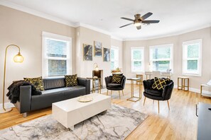 Ein modernes Wohnzimmer mit einem schwarzen Ledersofa, zwei schwarzen Sessel, einem weißen Couchtisch und einem Deckenventilator.