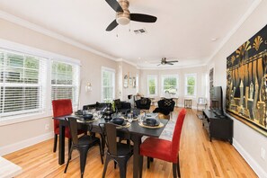 A dining area with a table set for four, chairs, a ceiling fan, and a large painting on the wall.