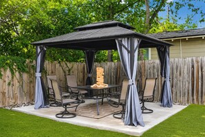 A covered patio area with a table and chairs, surrounded by a wooden fence and greenery.