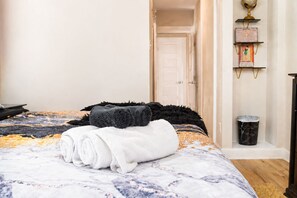 Ein ordentlich bezogenes Bett mit einer gemusterten Tagesdecke, einem gefalteten weißen Handtuch und einer schwarzen Decke.