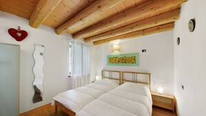 Un dormitorio con techo de madera, una cama, una mesita de noche con lámpara, un reloj de pared y un espejo.