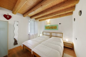 A bedroom with a wooden ceiling, a bed, a nightstand with a lamp, a wall clock, and a mirror.