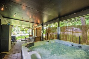 A covered outdoor hot tub area with a table and chairs, surrounded by a bamboo fence, and a view of a forested area.