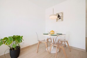 A dining area with a round table, clear chairs, a potted plant, and a hanging light fixture. - Apartment 'Joya' with Shared Pool, Wi-Fi and Air Conditioning (Torremolinos)