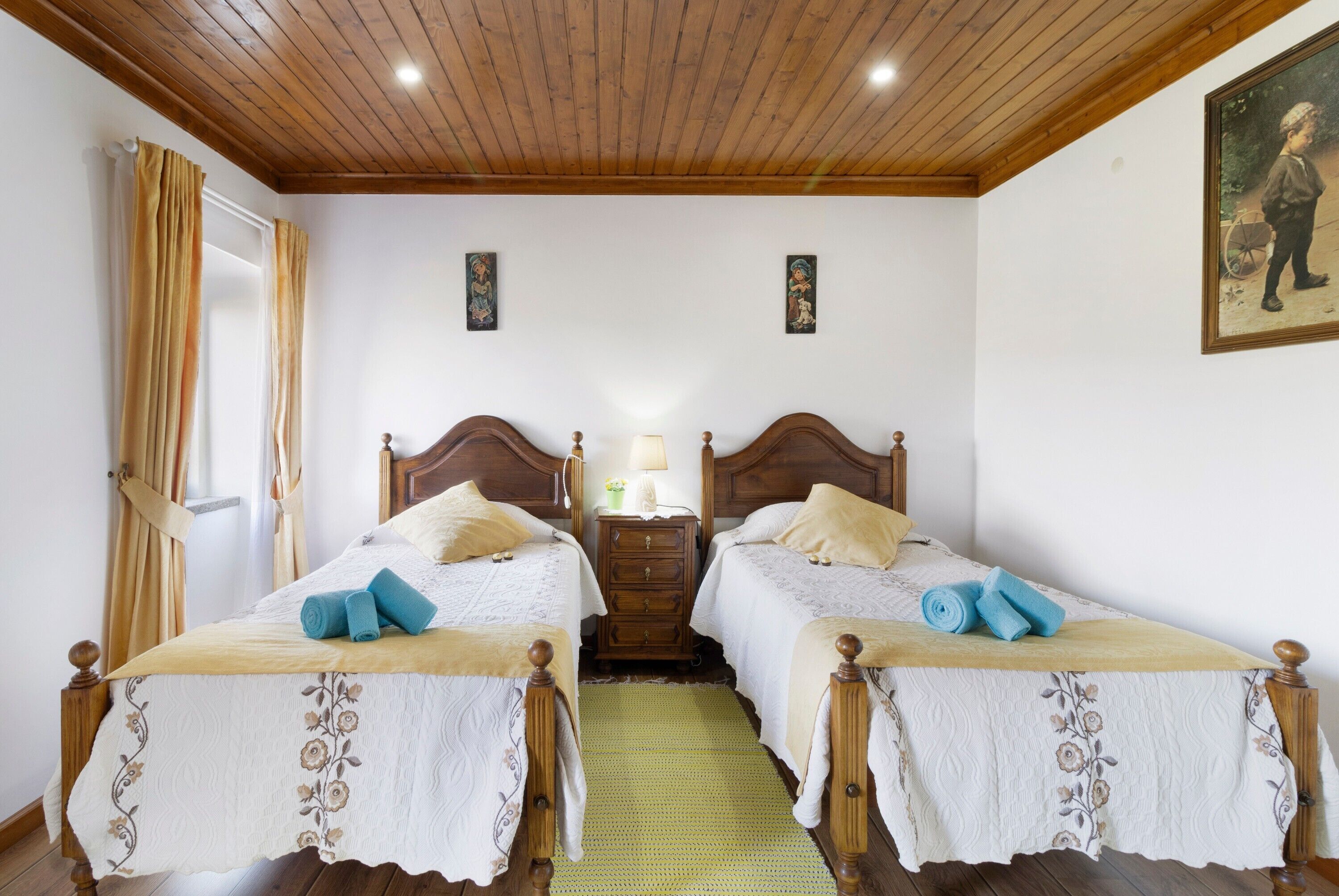 Habitación doble con dos camas, cabeceros de madera, un tapete verde, una mesita de noche con lámpara y un cuadro en la pared.