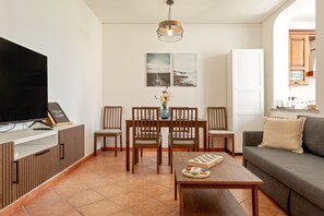En stue med fjernsyn, spisebord, stole, sofa og billedkunst på væggen.