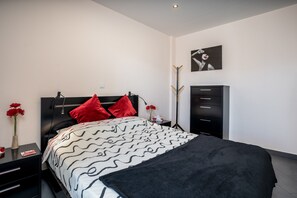 Une chambre à coucher moderne, comprenant un lit, des tables de chevet, une commode et une œuvre d’art accrochée au mur.