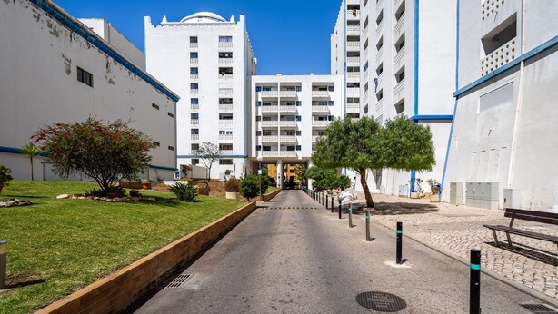 A pathway leading to a building with multiple floors, a grassy area with trees, and a clear blue sky. - Apartment 'Carpe Diem' with Balcony, Wi-Fi and Air Conditioning (Portimão)