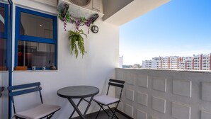A balcony with two chairs, a small table, a window with blue trim, and a city view. - Apartment 'Carpe Diem' with Balcony, Wi-Fi and Air Conditioning (Portimão)