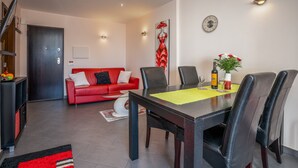 A dining area with a table, chairs, a red sofa, a clock, and a wall-mounted artwork. - Apartment 'Carpe Diem' with Balcony, Wi-Fi and Air Conditioning (Portimão)