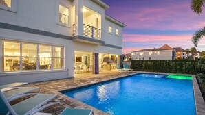 Une maison moderne à deux étages, dotée d’une piscine, d’un espace extérieur aménagé et d’un patio bien éclairé.