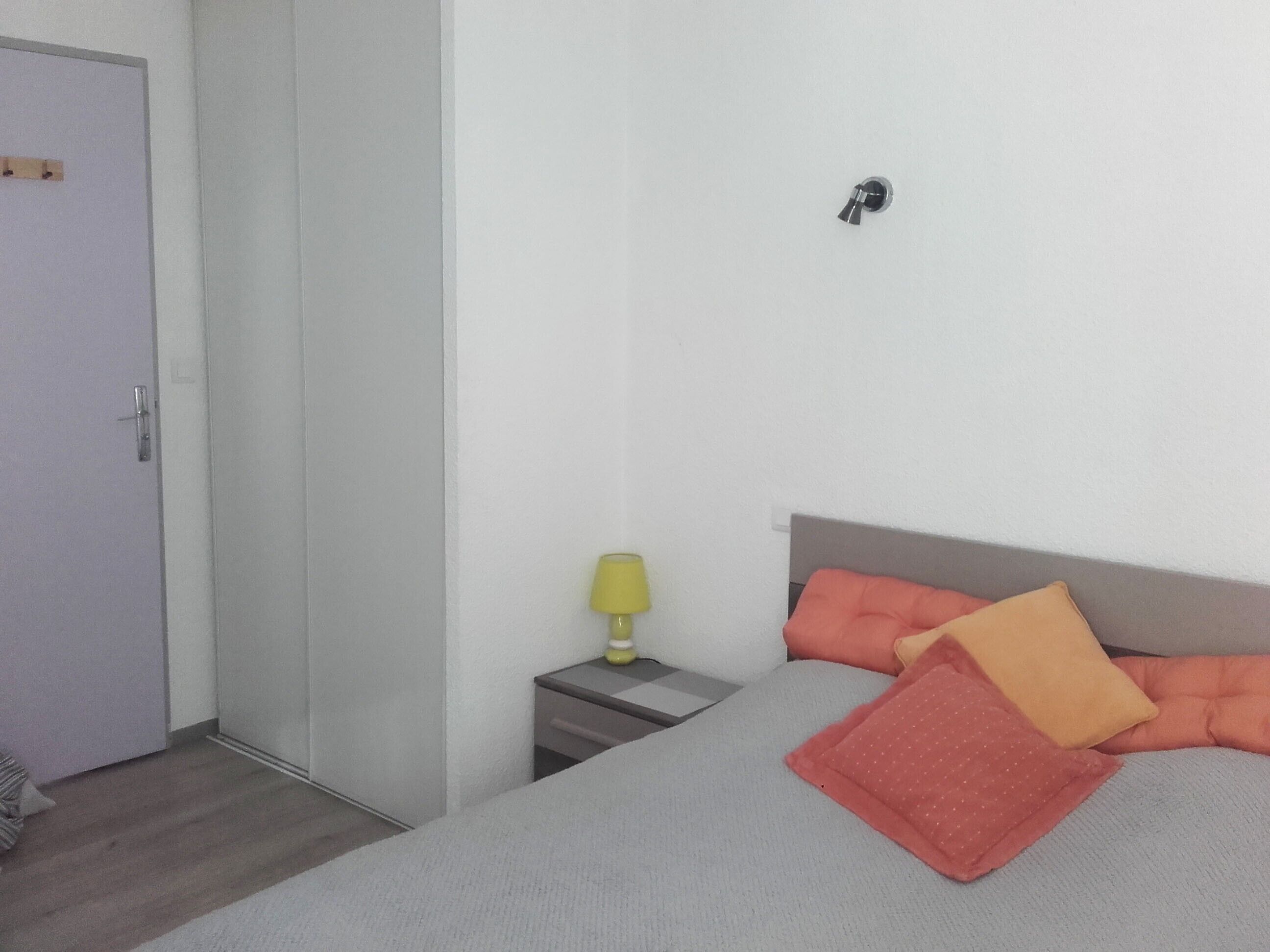 A bedroom with a bed, a nightstand, a lamp, and a door.